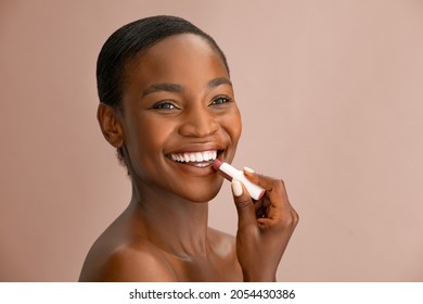 Cheerful beautiful woman applying natural lip balm brown background with copy space. Portrait of black woman applying lipstick while smiling. African american lady applying balm to her lips isolated. - Shutterstock ID 2054430386