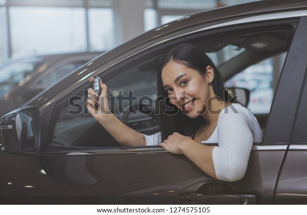 Cheerful\
beautiful woman smiling happily, holding car key sitting in her new\
automobile at dealership salon. Lovely female driver buying new\
car. Ownership, insurance, travelling\
concept