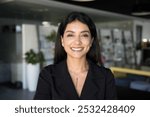 Cheerful beautiful young Arab entrepreneur woman in European casual cloth posing in office hall, looking at camera, smiling. Successful Middle Eastern businesswoman professional head shot portrait