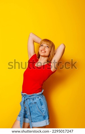 Cheerful beautiful young blond woman wearing trendy summer wear on yellow colored background