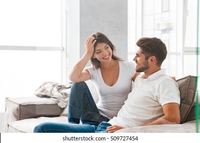 Cheerful Beautiful Young Couple Sitting And Talking On Sofa At Home