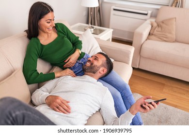 Cheerful beautiful young couple smiling and watching TV at home. Smiling young couple relaxing and watching TV at home
