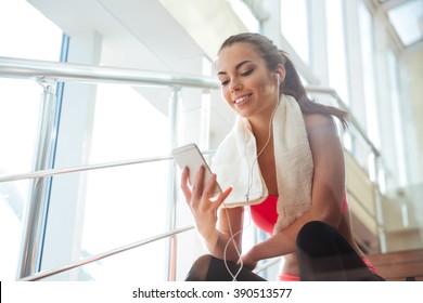 Cheerful beautiful young woman sitting on stairs in gym and listening to music  - Powered by Shutterstock