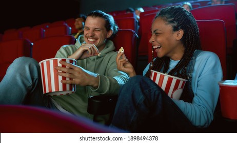 Cheerful best friends laughing, having popcorn while watching movie together, sitting in cinema auditorium. Entertainment and people concept. Web Banner - Powered by Shutterstock