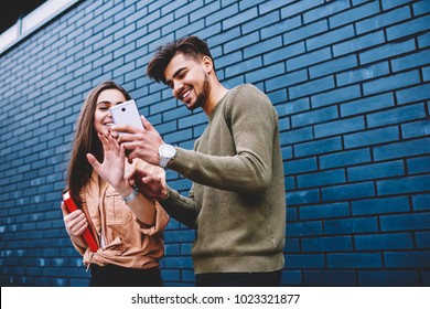 Cheerful Best Friends Viewing Funny Photos In Social Networks Via Smartphone Standing Together On Street, Happy Male And Female Hipsters Watching Funny Online Video Content On Mobile Phone Outdoors