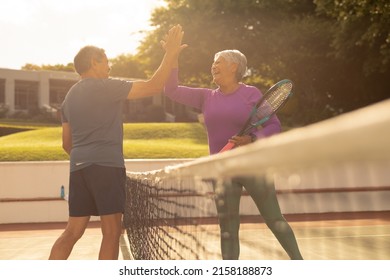 Cheerful biracial senior couple giving high-five while playing tennis at court during sunset. unaltered, sunlight, sport, competition, togetherness, love, retirement, healthy and active lifestyle. - Powered by Shutterstock