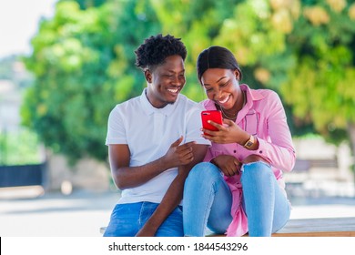 Cheerful Black couple hanging out at a park and looking at phone - Powered by Shutterstock