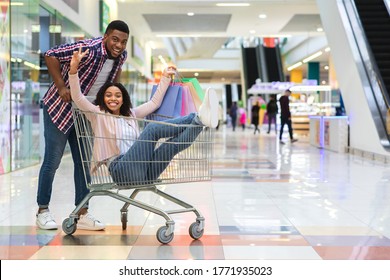 Cheerful Black Couple Having Fun After Successful Shopping In Mall, Riding Trolley And Laughing Together