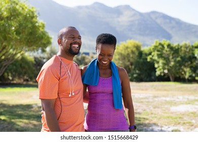 Cheerful Black Couple Resting Together After Jogging In The Park. Happy Mature Man And Woman Laughing While Resting After Running. Smiling Woman And Man Taking A Break After Fitness Training.