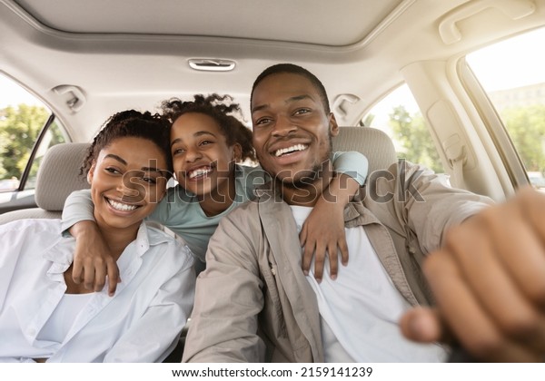 Cheerful Black Family Embracing Sitting In New\
Car Driving And Enjoying Road Trip On Summer Vacation. Parents And\
Daughter Posing In Auto. Automobile Rent And Purchase,\
Transportation Concept