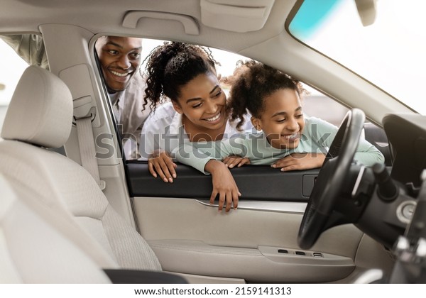 Cheerful Black Family Of Three\
Buying New Car, Looking Through Window At Auto Interior Choosing\
Luxury Automobile In Dealership. Vehicle Rent And Purchase\
Concept