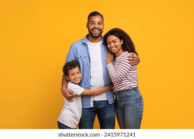 Cheerful black family of three with little son sharing loving embrace, happy african american father mother and male kid smiling at camera, standing against warm yellow background, copy space - Powered by Shutterstock