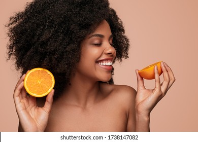 Cheerful Black Female With Curly Hair And Cut Orange Smiling With Closed And Enjoying Vitamin C Benefits For Skin Against Brown Background