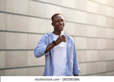 Cheerful Black Guy Drinking Clear Water From Bottle On City Street