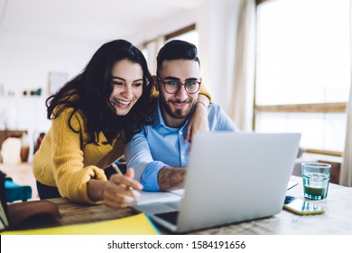 Cheerful Black Haired Woman Hugging Handsome Man In Fancy Glasses, Watching Funny Video On Laptop After Work And Laughing At Home 