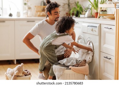 Cheerful Black Kid Boy Helping Father At Linen In Basket While Doing Laundry Near Washing Machine In Flight Kitchen In Weekend At Home  