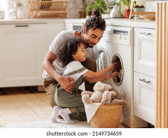 Cheerful black kid boy helping father at linen in basket while doing laundry near washing machine in flight kitchen in weekend at home   - Shutterstock ID 2149734659