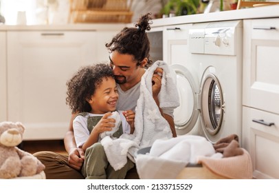 Cheerful Black Kid Boy Smiling  Dad And Helping Father At Linen In Basket While Doing Laundry Near Washing Machine In Flight Kitchen In Weekend At Home  