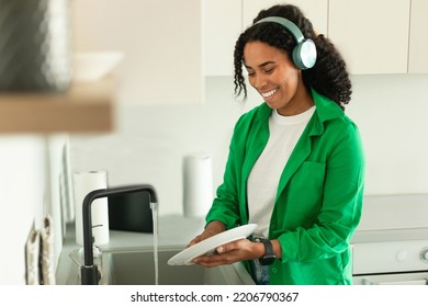 Cheerful Black Lady Doing Dishes Wearing Wireless Headphones Listening To Music In Modern Kitchen At Home. Female Doing House Chores Enjoying Favorite Songs Concept. Selective Focus - Shutterstock ID 2206790367