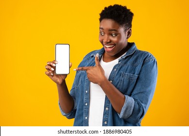 Cheerful Black Lady Showing Smartphone Blank Screen Recommending Application Posing Standing Over Yellow Studio Background. Mobile Application Ad. Check This App Concept. Mockup