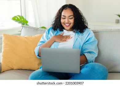 Cheerful Black Lady Using Laptop Computer Watching Movie Sitting On Sofa At Home. Freelancer Woman Working, Communicating And Learning Online. Internet Technology And Freelance Concept