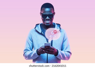 Cheerful black male influencer in shades and earbugs browsing social media pages on smartphone, celebrating new subscribers, notification with number of followers popping up from screen. Neon light - Powered by Shutterstock