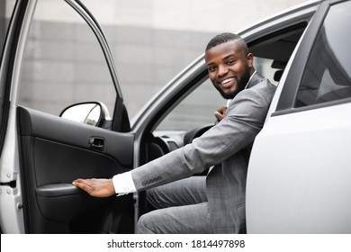 Cheerful black man in expensive suit getting in luxury car, holding door and smiling at camera. African american successful entrepreneur going to office in the morning