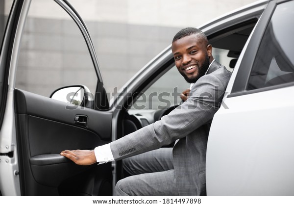 Cheerful black man in expensive\
suit getting in luxury car, holding door and smiling at camera.\
African american successful entrepreneur going to office in the\
morning