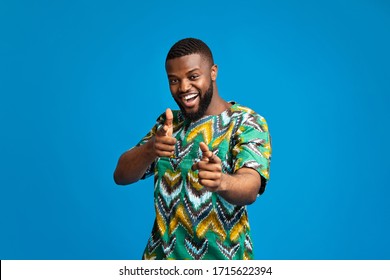 Cheerful black man in traditional african clothes indicating to camera over blue