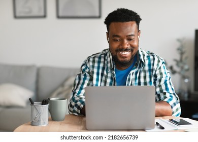 Cheerful Black Man Using Laptop Working Distantly Online Sitting At Desk At Home. Freelancer Guy Browsing Internet. Freelance Career And Remote Job, Technology Concept