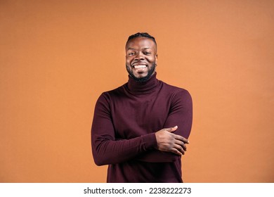 Cheerful black man wearing black leather jacket smiling in studio shot and looking at camera against brown background.