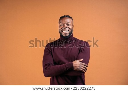 Cheerful black man wearing black leather jacket smiling in studio shot and looking at camera against brown background.