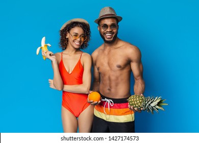 Cheerful Black Man And Woman Enjoying Fresh Summer Fruits, Blue Studio Background