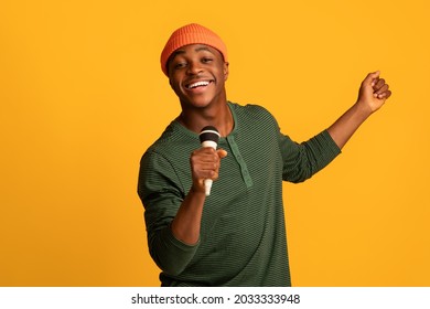 Cheerful Black Millennial Guy Holding Microphone And Singing At Camera, Young Joyful African American Hipster Man Enjoying Karaoke, Having Fun While Standing Over Yellow Studio Background, Copy Space - Powered by Shutterstock