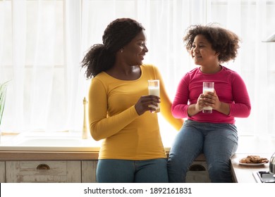 Cheerful Black Mom And Daughter Drinking Milk And Eating Cookies In Kitchen, Happy African American Family Having Healthy Snacks And Bonding At Home, Cute Little Girl Sitting On Table, Copy Space