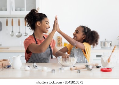 Cheerful Black Mother And Daughter Giving High Five While Cooking At Home, Wearing Aprons, Happy African American Family Baking Cookies Together At Kitchen, Cheering Each Other, Copy Space
