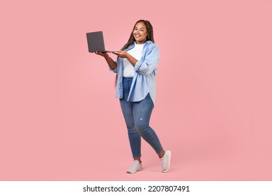 Cheerful Black Overweight Freelancer Lady Using Laptop Computer Working Online Posing Standing Standing Over Pink Studio Background. Internet Technology Concept. Full Length Shot