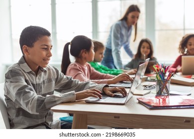 Cheerful Black Schoolboy Using Laptop Computer Learning Online With Diverse Classmates Sitting At Desk In Modern Classroom At School. E-Learning, Technology And Education Concept - Powered by Shutterstock