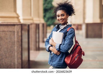 Cheerful Black Student Girl Hugging Books Posing With Backpack Near College Building Outdoor, Smiling To Camera. Modern Education, College Tuition And Grants, Studentship And Study Abroad Concept - Shutterstock ID 2026823639