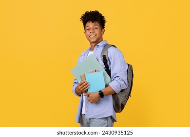 Cheerful black student guy with stylish haircut and backpack confidently holds textbooks, ready for day of learning against vibrant yellow background - Powered by Shutterstock