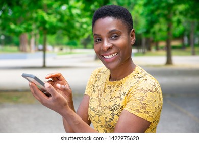 Cheerful Black woman checking social media on smartphone. Portrait of beautiful attractive African-American young woman using mobile application when resting in park. Technology concept - Shutterstock ID 1422975620