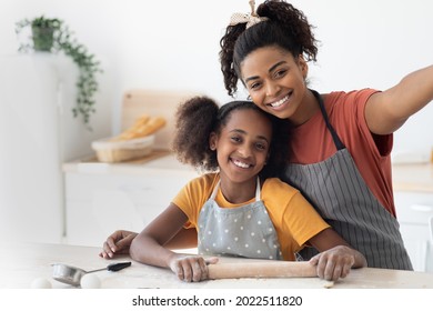 Cheerful Black Young Mother And Teen Daughter Taking Selfie While Cooking Together At Home, Happy African American Mom And Kid Wearing Aprons, Rolling Dough For Pie Or Cookies, Copy Space