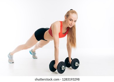 cheerful blond athlete with straight arms holding dumbbells and leaning with them on the floor. full length side view shot