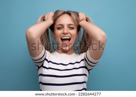 cheerful blond young woman holds her hair in her hands and laughs cutely on a blue background