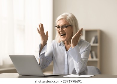 Cheerful blonde elderly business woman celebrating professional success, working at laptop, laughing, shouting for joy at home office workplace, getting good news from video call - Powered by Shutterstock