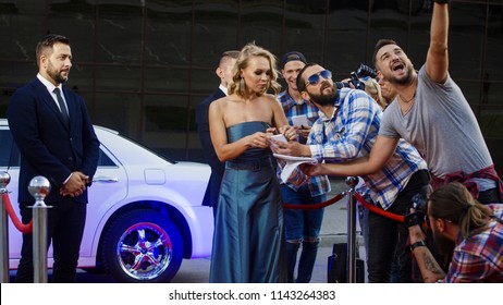 Cheerful Blonde Woman In Gray Dress Getting Out Of Limousine And Giving Autographs To Fans On Red Carpet