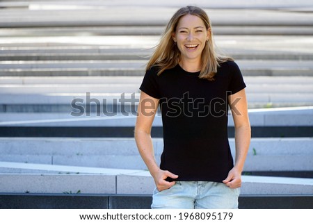 Cheerful blonde woman outdoors wearing black t-shirt with copy space or text space for print or design                             