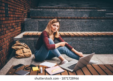 Cheerful Blonde Woman Student In Casual Clothes With Backpack Has Video Call On Laptop On Stone Step Of Bench Cascade