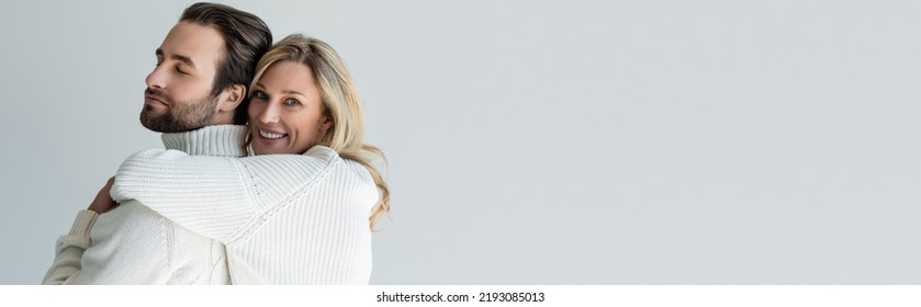cheerful blonde woman in white knitted sweater hugging bearded man isolated on grey, banner - Shutterstock ID 2193085013