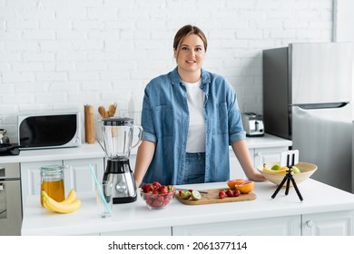 Cheerful Body Positive Woman Looking At Camera Near Fruits, Honey And Smartphone In Kitchen